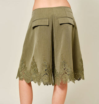 Model facing away from the camera wears wide-legged olive green shorts with lace hem detail and back pocket flaps