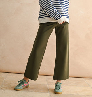 Model wears a pair of cropped flared olive green pants with a white and navy striped sweater and teal and pink sneakers