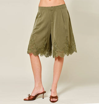 Model wears olive green wide-legged knee-length shorts with lace hem detail paired with a pair of open-toed brown kitten heels with bow accents