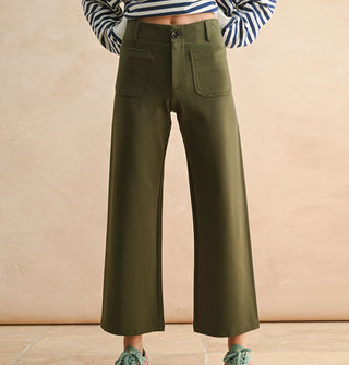 Model wears a pair of cropped flared olive green pants with pockets, belt loops, and button closure