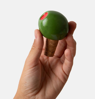A model's hand holds a green ceramic pimento olive and cork bottle stopper