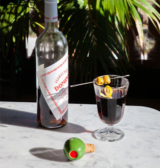 Olive bottle stopper rests on a marble surface with cocktail glass and bottle