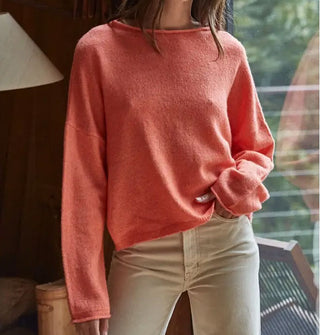 Model wears a slouchy salmon-colored sweater with rolled boat neckline