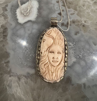 Carved bone pendant in silver setting features design of woman's face with flowing hair and a horse's face above and to the side