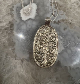 Reverse side of silver necklace pendant features ornate floral engraving