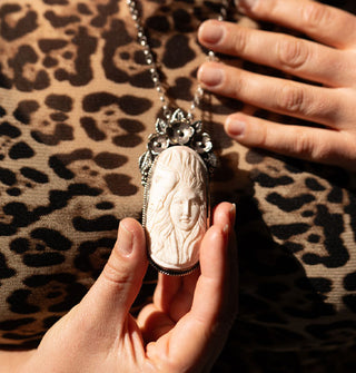 Model in leopard print top holds the oblong white carved bone pendant in a floral silver setting on a silver chain