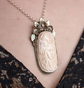 Oblong carved white bone pendant depicting a woman's face and horse's face in a silver setting of three flowers with leaves on thin silver belcher chain