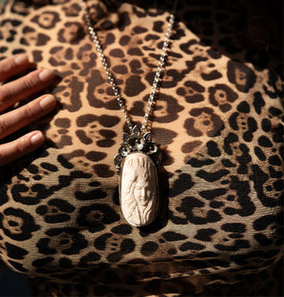 Model in leopard print top wears an oblong white carved bone pendant in a floral silver setting on silver chain around neck