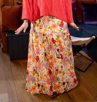 Model with hands splayed wears a brightly colored floral maxi skirt with red cable knit sweater
