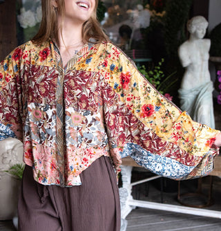 Smiling model with arms outstretched wears a button-down shirt with patchworked floral prints and billowy sleeves