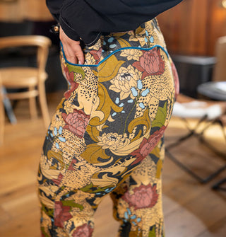 Model wears a pair of corduroy pants with cheetah and floral print accented with blue velvet piping along the hip