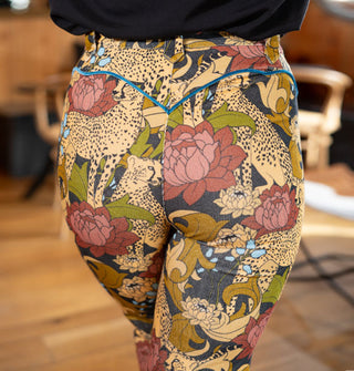 Model wears a pair of corduroy pants with cheetah and floral print accented with blue velvet piping along the hip