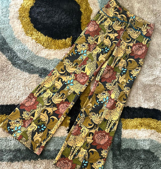 Pair of pants featuring an intricate print of cheetahs and flowers lay flat on a retro-style rug
