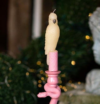 A parrot-shaped taper candle with pink base that resembles tree bark is placed in a pink holder wrapped in a snake figurine