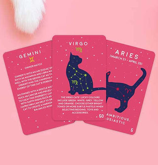 Three sample cards from the Paw-Mistry: Cat Edition deck are fanned out on a pink surface with white furry cat's tail tip at upper left