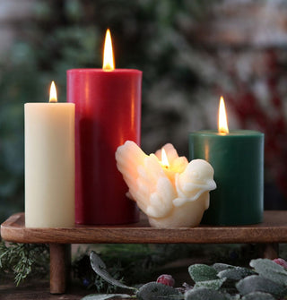 Lit white beeswax dove candle with other lit pillar candles on a wooden tray staged with greenery