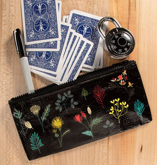 Black rectangular zippered pouch with colorful plant illustrations spills out playing cards, padlock, and permanent marker onto a wooden surface