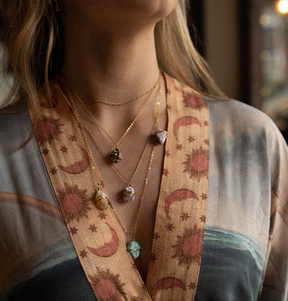 Model in sun, moon, and star print robe wears a layered crystal necklace on gold chain