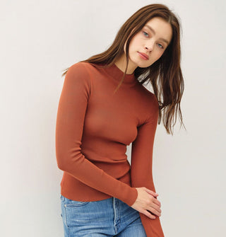 Model wears a long-sleeved rust-colored mock turtleneck top with blue jeans