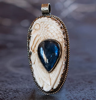 Oval carved bone pendant depicting a phoenix's head with blue labradorite upside-down teardrop inset in a silver border with top-set rounded bail