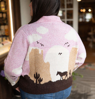 Model wears a collared sweater with a pink, white, tan, and brown desert landscape scene