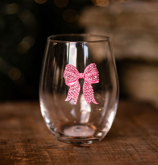 Clear stemless wine glass resting on a wooden surface features a pink bow accent covered in pink rhinestones