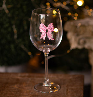 Clear wine glass resting on a wooden surface features a pink bow accent covered in pink rhinestones