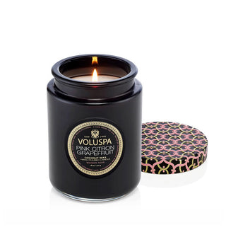 Black glass Pink Citron Grapefruit Voluspa candle jar with one lit wick inside and patterned tin lid set to one side
