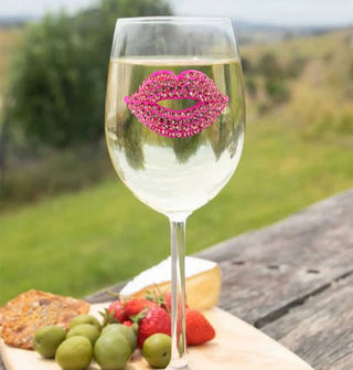Wine glass with bejeweled pink lips decal is staged on a charcuterie board against a pastoral backdrop