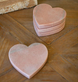 Four pink heart-shaped marble drink coasters on a wooden tabletop, three stacked and one set to the foreground