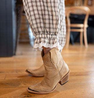 Closeup of the lace trim around the ruffled, elasticated ankle cuffs of a pair of plaid pants worn with tan cowgirl boots
