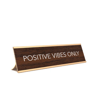 Rectangular faux brown wood finish desk plate sign with gold top and bottom frame says, "Positive vibes only" in white lettering