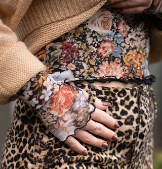 Model wears a long-sleeved floral print top with lettuce edges and thumbholes paired with a tan sweater and leopard print pants
