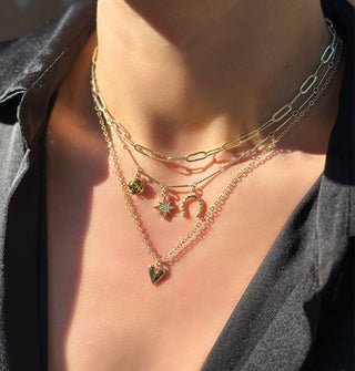 Model wears three gold necklaces: one large chain, one three-pendant link chain, and one mini heart pendant on standard chain
