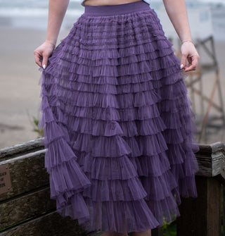 Model wears a multi-tiered ruffled purple tulle maxi skirt on a beach boardwalk