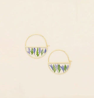 Gold hoop earrings with bottom semicircles containing resin-encased pressed purple flowers and green leaves