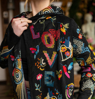 Model wears a black cardigan with colorful embroidered designs and the word, "Love" in large letters