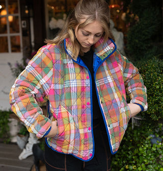 Model pulls hands from the pockets of a plaid quilted jacket with rainbow color palette and blue lining and piping 