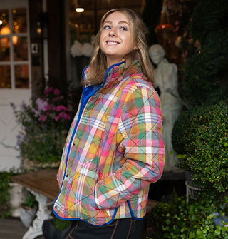 Smiling model poses with hands in the pockets of a plaid quilted jacket with rainbow color palette and blue lining and piping 
