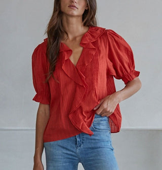 Model wears a ruffly red blouse with pleated details and short balloon sleeves