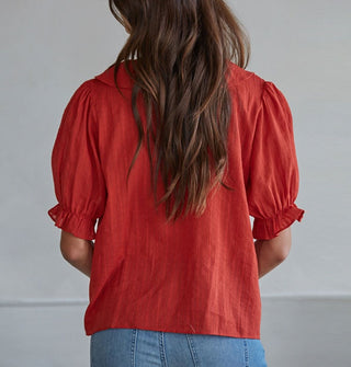 Model with back to camera wears a ruffly red blouse with short balloon sleeves