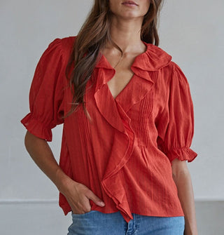 Model with one hand in jeans pocket wears a ruffly red blouse with pleated details and short balloon sleeves