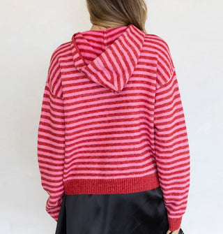Model facing away from the camera wears a red and pink striped zip-front hooded sweatshirt