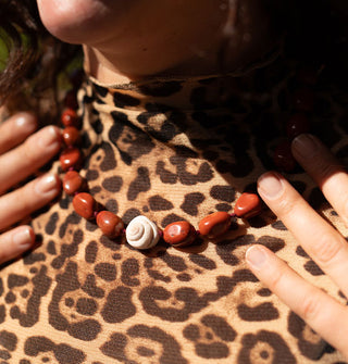 Model in leopard print shirt wears a necklace strung with polished red jasper stones and a central white accent seashell