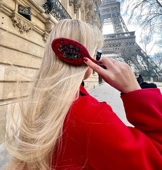 Model runs a red quartz snake brush through long blonde hair in front of the Eiffel Tower