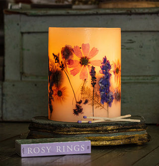 Lit botanical candle staged with matchsticks and matchbox on a rusticated platform features inlaid flowers and leaves lit from within