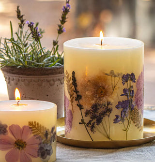 Two lit single-wick botanical pillar candles on a tabletop with potted lavender