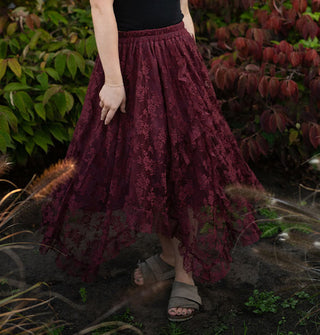 Model standing among lush greenery twirls in a midi-length wine red lace handkerchief skirt