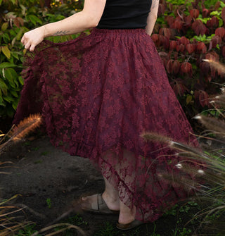 Model standing among lush greenery twirls in a midi-length wine red lace handkerchief skirt