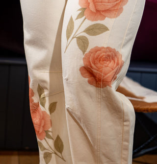Closeup of the seams and darts on the legs of a pair of white barrel jeans with rose designs